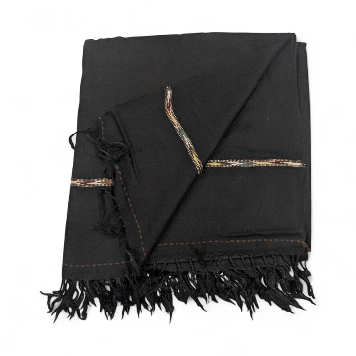 A pure pashmina shawl in black, folded and draped, featuring subtle narrow border details with hints of red, yellow, and white stitching, and fringed edges, displayed on a white background.