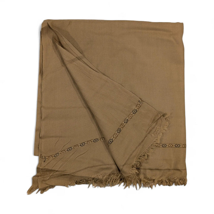 A pure pashmina shawl in a light brown or tan color, folded and draped, featuring subtle dark patterned border details and fringed edges, displayed on a white background.