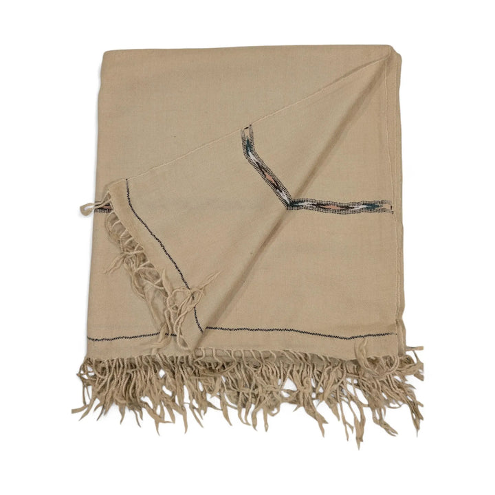 A pure pashmina shawl in a light beige or off-white color, folded and draped, featuring subtle dark blue and red patterned border details and fringed edges, displayed on a white background.